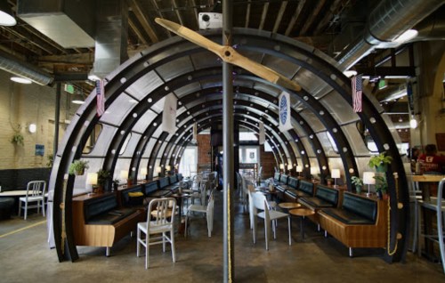 Interior of a unique restaurant with an arched metal design, featuring booths, tables, and decorative propeller.
