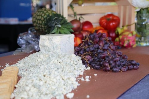 A spread of blue cheese, grapes, and fresh fruits like pineapple and tomatoes on a wooden table.