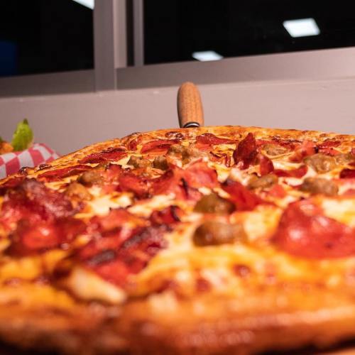 A close-up of a pepperoni pizza with green olives, fresh out of the oven, on a wooden board.