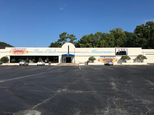 Exterior of the Alabama Fan Club and Museum, featuring a large sign and parked cars in a sunny parking lot.
