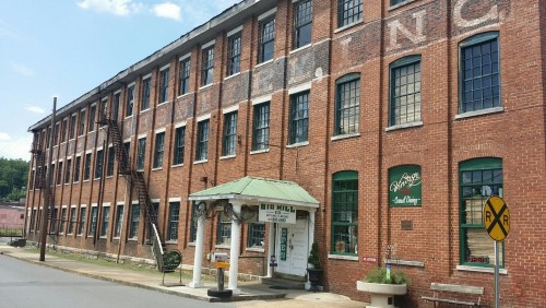 Historic brick building with large windows, featuring a green awning and a sign for "Big Mill" near a railroad crossing.