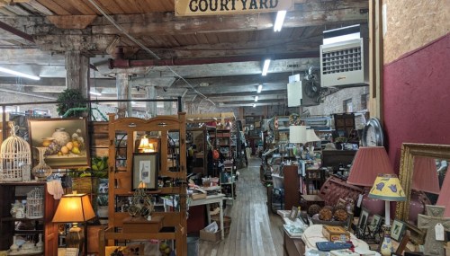 A spacious antique store filled with various vintage items, furniture, and decor under wooden beams and a sign reading "Courtyard."