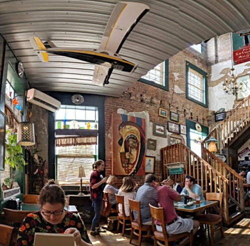 A lively restaurant interior with a model airplane hanging from the ceiling, featuring colorful decor and diners at tables.