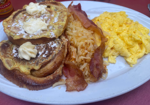 A plate of breakfast featuring French toast with butter, crispy bacon, scrambled eggs, and hash browns.