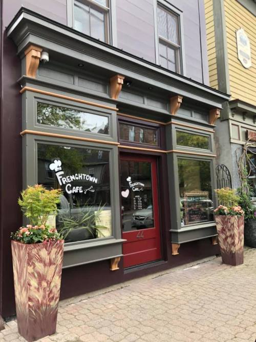 Exterior of a cafe with large windows, a red door, and decorative planters on either side. Sign reads "Frenchtown Cafe."