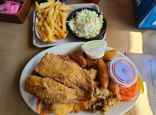 A plate of fried fish, shrimp, hushpuppies, coleslaw, fries, and a side of dipping sauce.