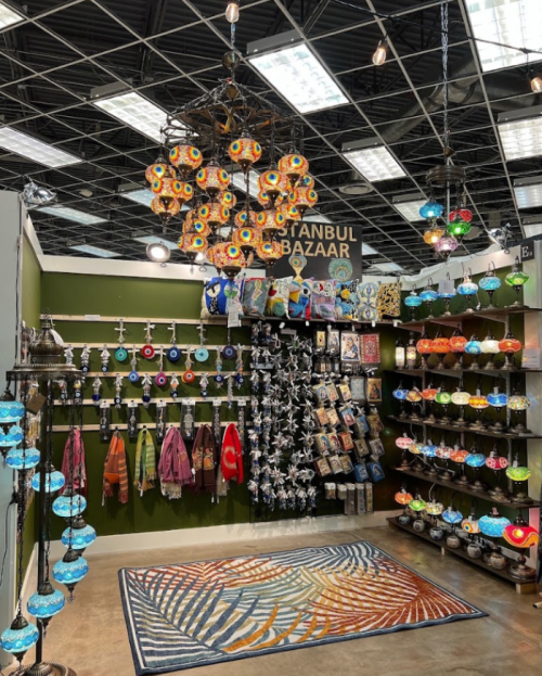 A vibrant market stall featuring colorful lamps, textiles, and decorative items, with a striking chandelier overhead.