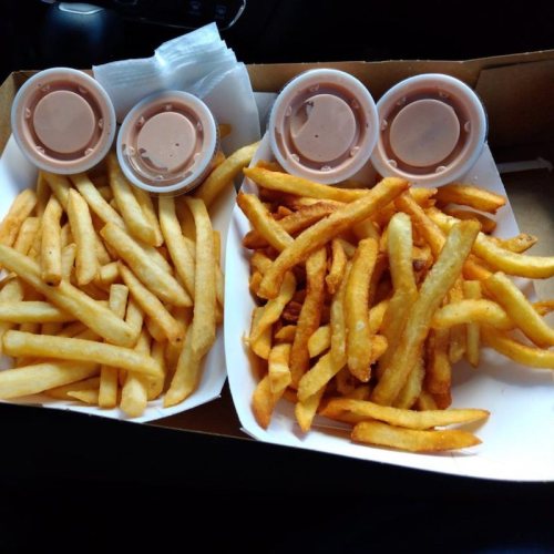 Two trays of French fries, one with regular fries and the other with crinkle-cut fries, accompanied by dipping sauces.