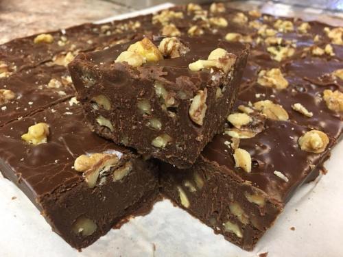 A close-up of rich chocolate fudge with walnuts, cut into squares and arranged on a surface.