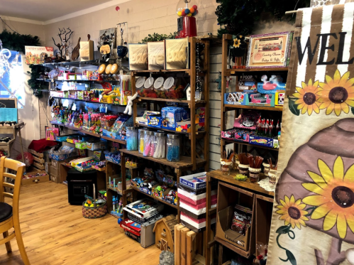 A colorful display of various candies and toys on wooden shelves in a cozy shop setting.