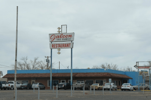 Sign for "Jalcon Family Restaurant" in front of a blue building with parked cars under a cloudy sky.