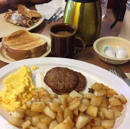 A breakfast plate with scrambled eggs, sausage patties, hash browns, toast, and a cup of coffee.