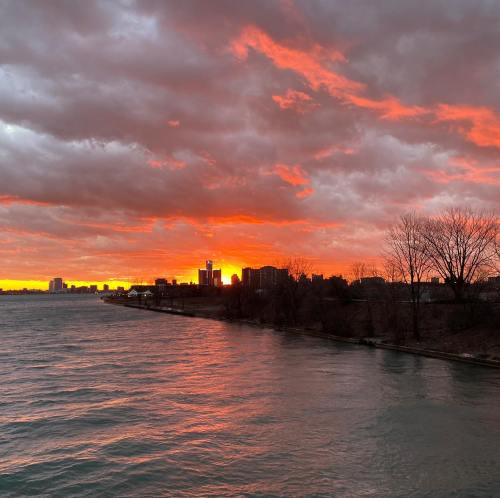 A vibrant sunset over a calm body of water, with dramatic clouds and city skyline in the background.