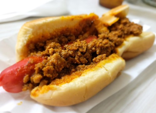 Two hot dogs in buns, topped with a generous portion of seasoned ground meat and sauce.