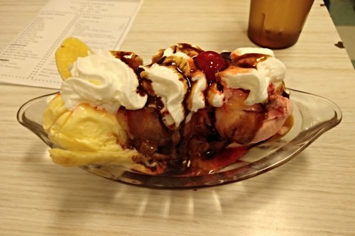 A colorful ice cream sundae with three scoops, whipped cream, chocolate sauce, cherries, and a slice of lemon.