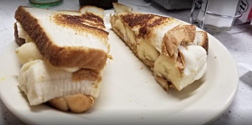 A plate with two toasted peanut butter and banana sandwiches, cut in half, showing the creamy filling.