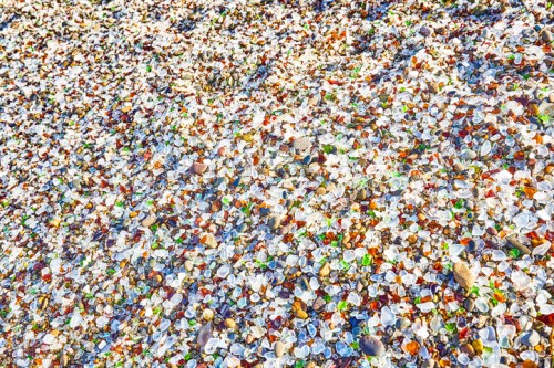 A colorful array of smooth, polished sea glass pieces scattered across a sandy surface.