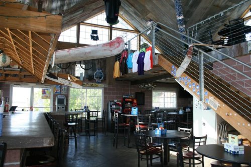 Interior of a rustic restaurant with wooden beams, a bar area, and colorful shirts hanging from the ceiling.