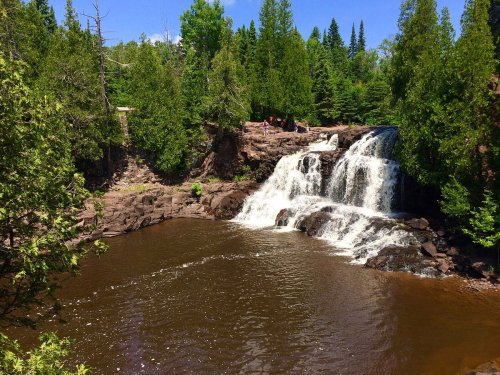 A scenic waterfall cascading into a calm pool, surrounded by lush green trees and rocky terrain.
