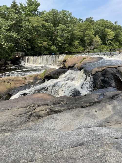 A serene waterfall cascades over rocky terrain, surrounded by lush green trees and a peaceful natural setting.