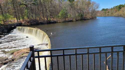 A serene river scene featuring a waterfall cascading over a dam, surrounded by trees and clear blue skies.