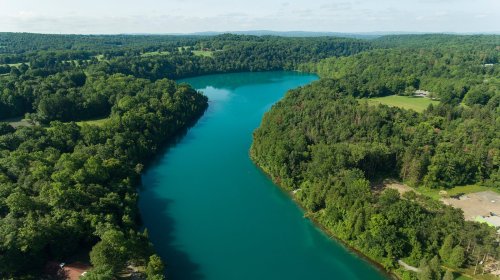 Aerial view of a winding river surrounded by lush green forests and fields under a clear blue sky.