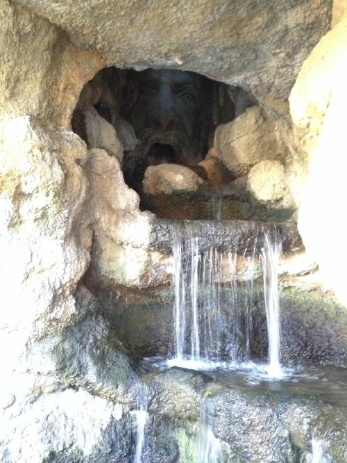 A rocky cave with a small waterfall, revealing a hidden face in the shadows.