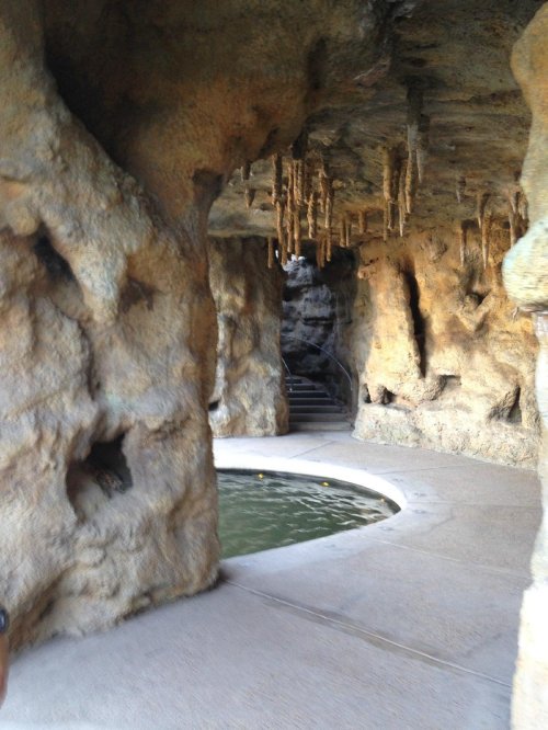 A rocky cave-like structure with a curved pool and stalactites hanging from the ceiling. Stairs are visible in the background.