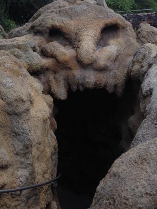 A rocky formation resembling a creature's face with a gaping mouth and expressive eyes, set in a natural landscape.