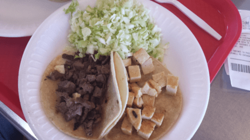 Two tacos on a plate: one with beef, one with grilled chicken, accompanied by a side of shredded lettuce.