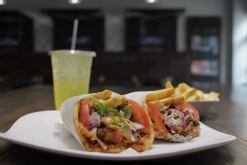 Two delicious wraps filled with meat, vegetables, and fries, served with a drink and a side of fries on a plate.