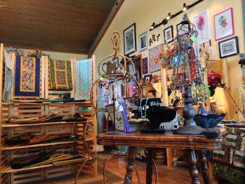 A cozy craft shop filled with colorful fabrics, handmade jewelry, and art displayed on walls and shelves.