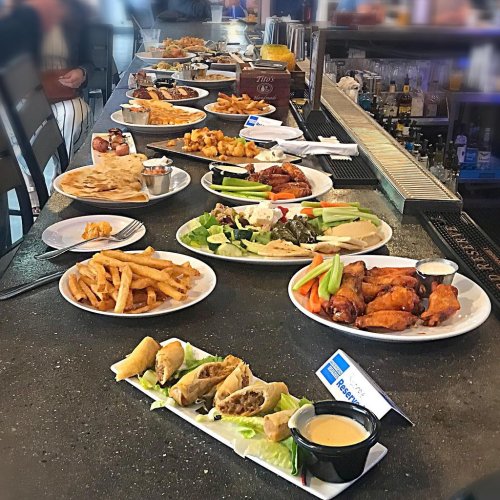 A variety of dishes on a bar counter, including wings, fries, salads, and appetizers, arranged on white plates.