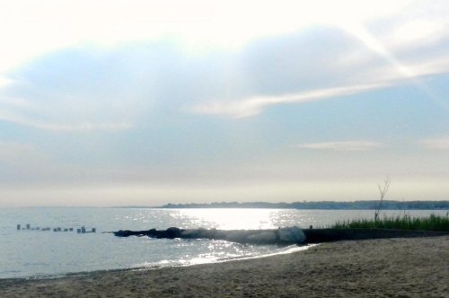 A serene beach scene with gentle waves, soft clouds, and sunlight reflecting on the water's surface.