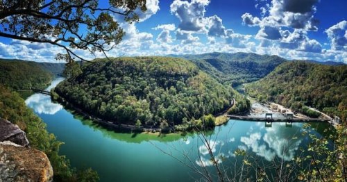 A scenic view of a river winding through lush green hills under a bright blue sky with fluffy clouds.