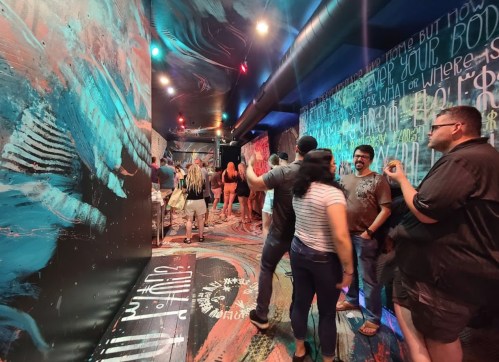 A vibrant hallway with colorful murals and people socializing, creating a lively atmosphere.