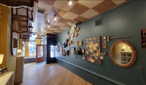 A cozy interior with a green wall, eclectic decor, and an upside-down ceiling featuring chairs and artwork.