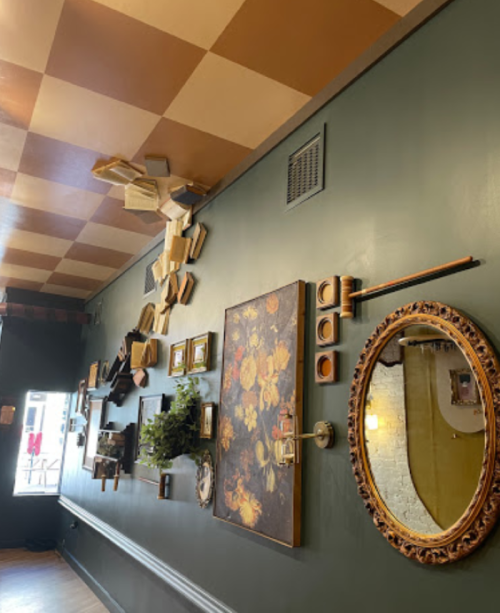 A creatively decorated wall featuring a mix of framed art, mirrors, and wooden elements against a dark green backdrop.