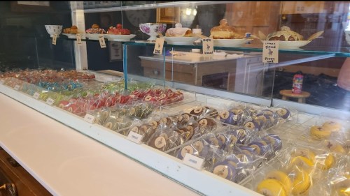 A display case filled with colorful macarons and pastries, labeled with small tags, in a cozy bakery setting.