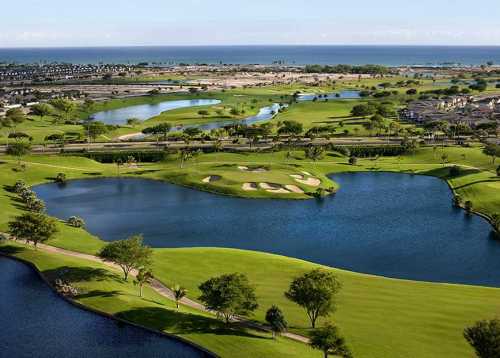 Aerial view of a lush golf course with water features and greenery, overlooking a coastal landscape.