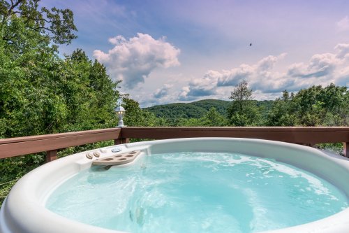 A hot tub on a deck overlooking lush green hills and a cloudy sky.