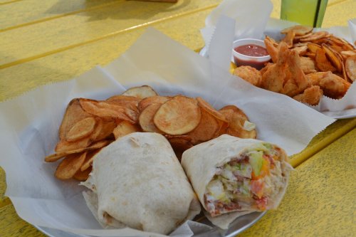 A plate with a wrapped burrito and a side of crispy potato chips, served with a small cup of salsa.