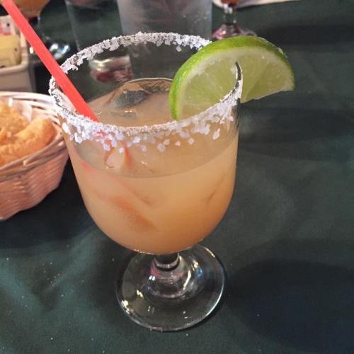 A refreshing cocktail in a glass with a salted rim, garnished with a lime slice and a straw, on a green tablecloth.