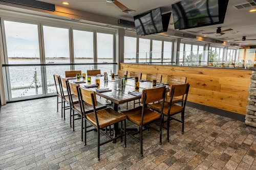 A dining area with a large table set for a meal, surrounded by windows overlooking a waterfront view.