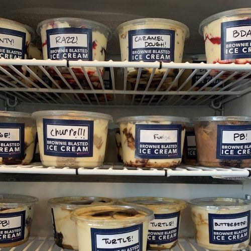 A freezer shelf filled with various flavors of ice cream in labeled containers, including "Brownie Blasted" and "Caramel Dough."