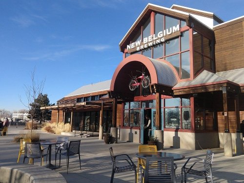 Exterior of New Belgium Brewing with a bike hanging above the entrance and outdoor seating in a sunny setting.