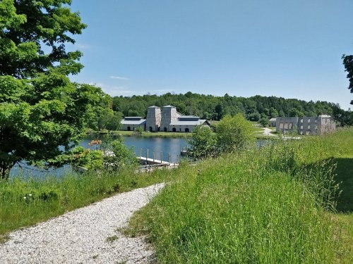 A scenic view of a lake surrounded by greenery, with buildings in the background under a clear blue sky.