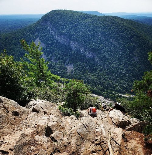 A scenic view from a rocky overlook, showcasing lush green mountains and a valley below under a clear sky.