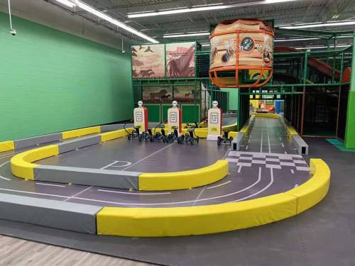 Indoor go-kart track with yellow barriers, checkered finish line, and a colorful backdrop.