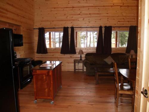 Cozy wooden cabin interior with a kitchen, dining table, sofa, and large windows letting in natural light.